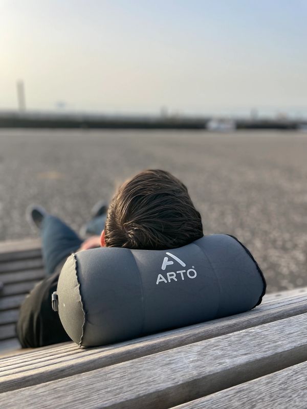 Man using the Arto Pillow - Inflatable while laying on a bench. 