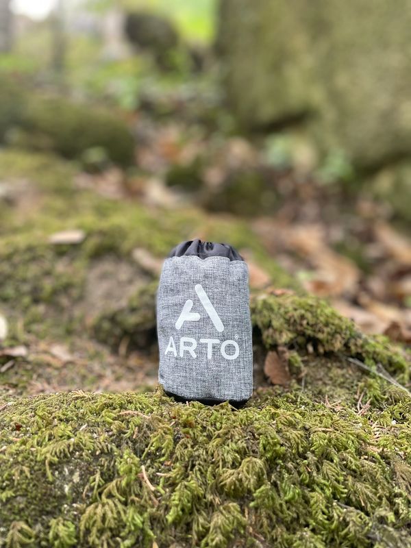 The Arto Pillow - Inflatable in it's carrying case, sitting on a grassy rock.