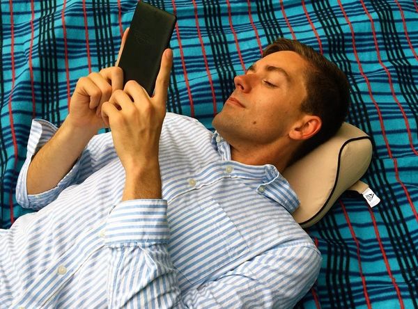 Man laying on the Arto Pillow - Memory Foam while reading at a picnic.