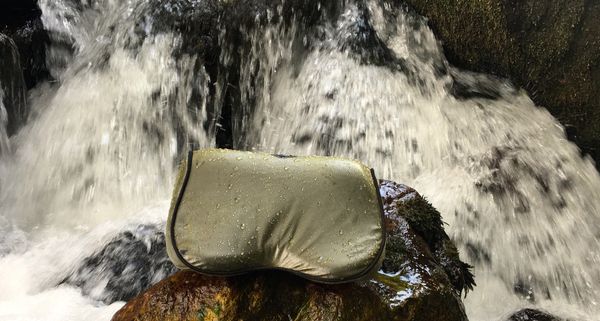 The Arto Pillow - Memory Foam + sitting in front of a waterfall with it's water resistant cover on.