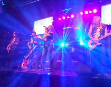 Rock band performing live on stage with vibrant blue and purple lighting.