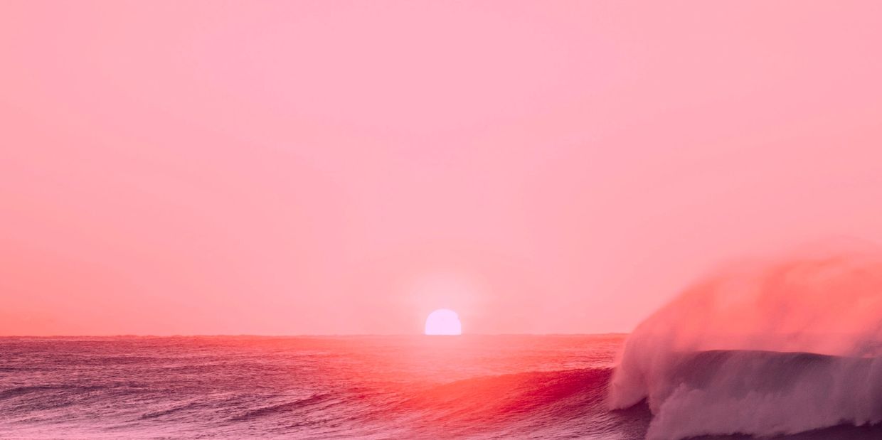 A vibrant pink sunset over ocean waves.