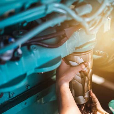 Hands holding a cup near a car engine with sunlight shining.