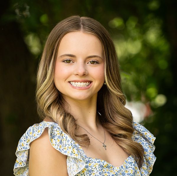 Young woman smiling outdoors with curled hair and floral dress.
