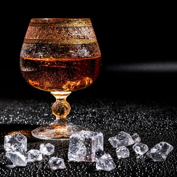 Elegant glass of amber liquid with scattered ice cubes on a dark surface.