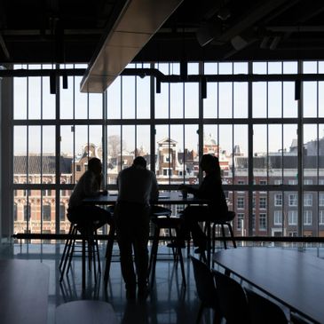 Silhouettes of three people chatting near a large window with city view.