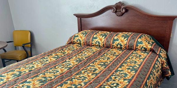Bed with ornate wooden headboard and patterned bedspread in a simple room.