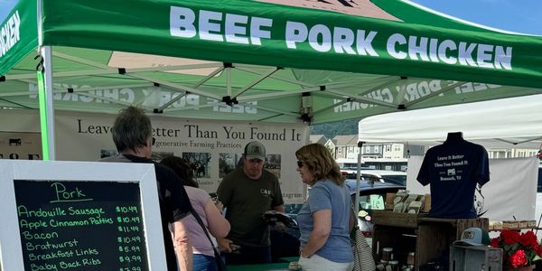 Farmers market stall selling pork products under a green tent.