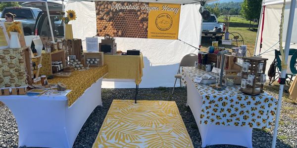 Outdoor market stall selling honey and bee-related products with sunflower decor.