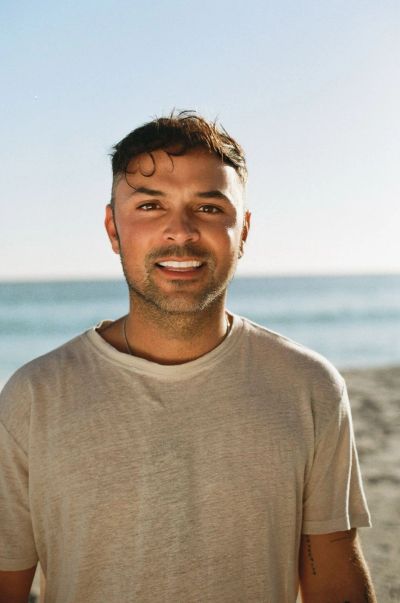 Smiling man in a beige t-shirt at the beach on a sunny day.