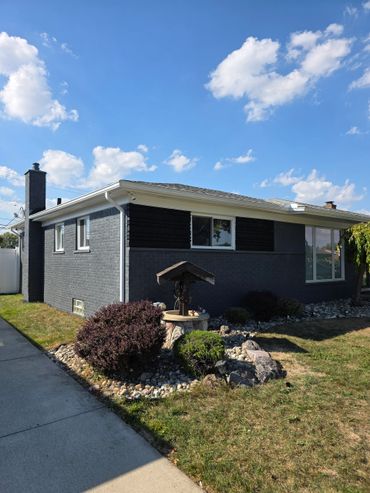 Gray brick house with a chimney and landscaped front yard under a blue sky.