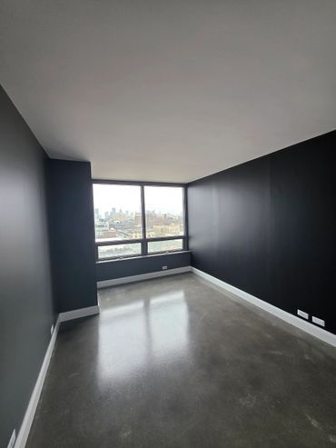 Empty modern room with dark walls, large window, and polished concrete floor.