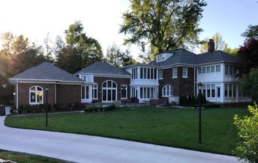 Large brick house with white trim surrounded by green trees and lawn.