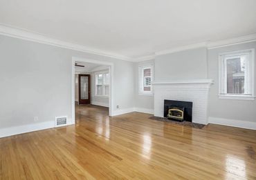 Bright empty living room with hardwood floors and a white fireplace.