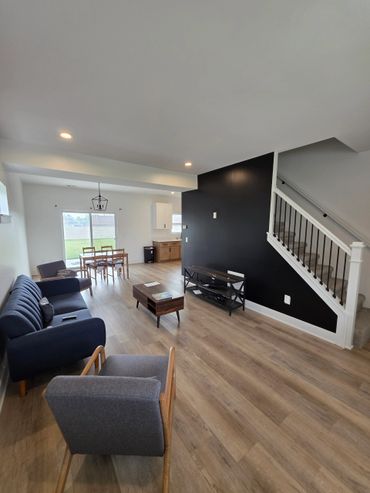 Modern living room with navy and gray chairs, black accent wall, and dining area.