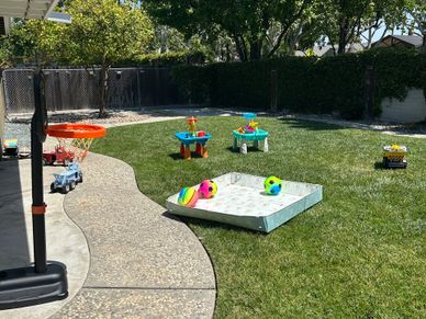 Backyard with kids' toys including basketball hoop and sandbox on a sunny day.