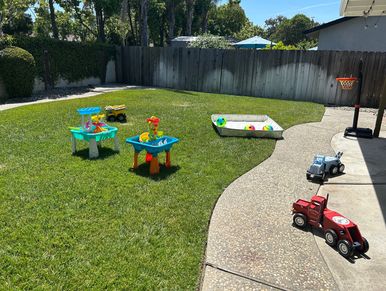 A backyard with kids' toys and a basketball hoop on a sunny day.