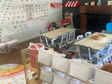 A colorful and organized preschool classroom with tables, chairs, and educational posters.
