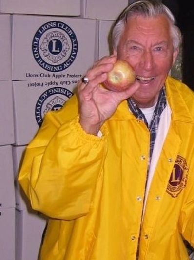 Smiling man in bright yellow Lions Club jacket with boxes of apples