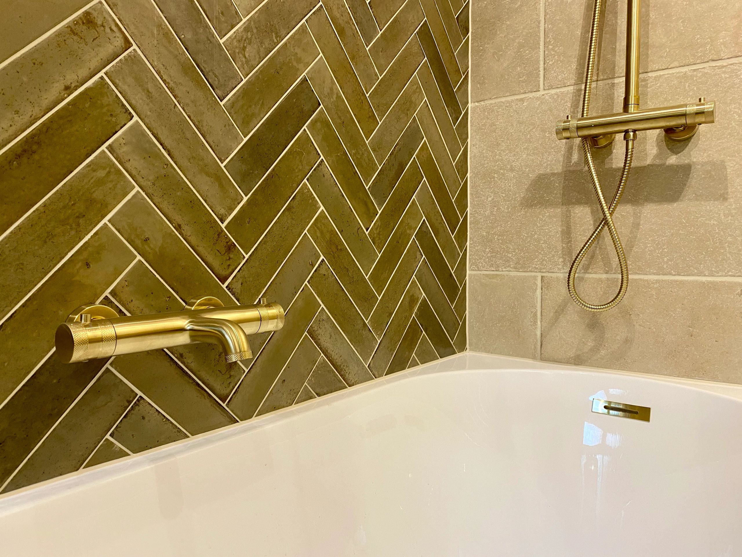 Gold shower fixtures with herringbone tiles and a white bathtub.