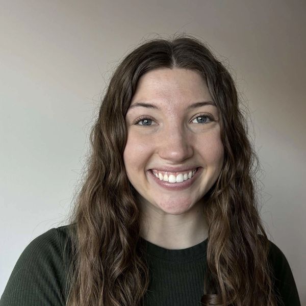 Young woman with long wavy hair smiles brightly against a plain background.
