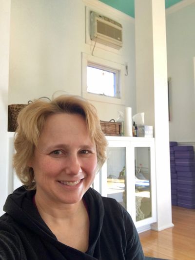 A photograph of a smiling woman in a yoga studio.