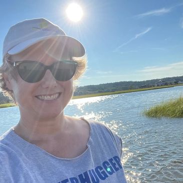 An image of a smiling woman in sunglasses beside a river.