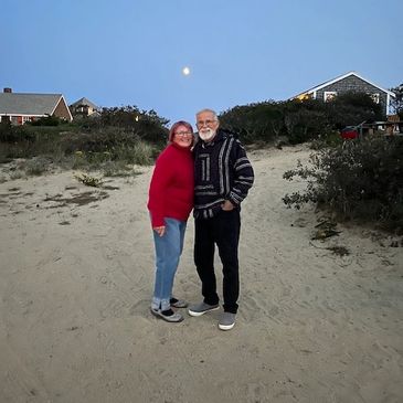 A photograph of a mature couple on a beach with a full moon in the background.