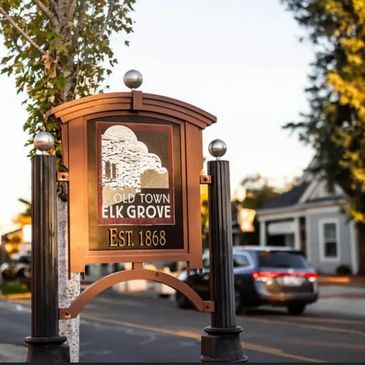 "Wooden sign for Old Town Elk Grove, established in 1868, with tree and building illustration."