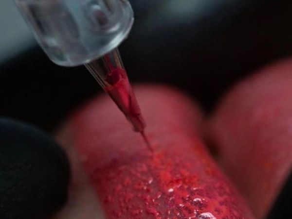 Close-up of a needle performing a cosmetic lip tattoo with red pigment for lip blush procedure.