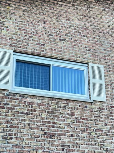 Ventana con persianas blancas sobre pared de ladrillo.