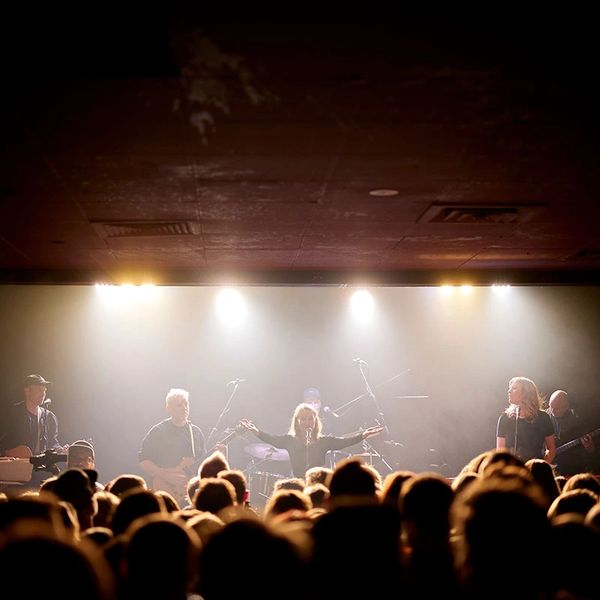 A live band performs on stage with bright lights and a cheering crowd.
