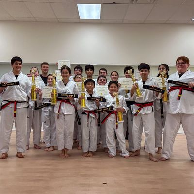 Karate students proudly display trophies and black belts in a dojo.