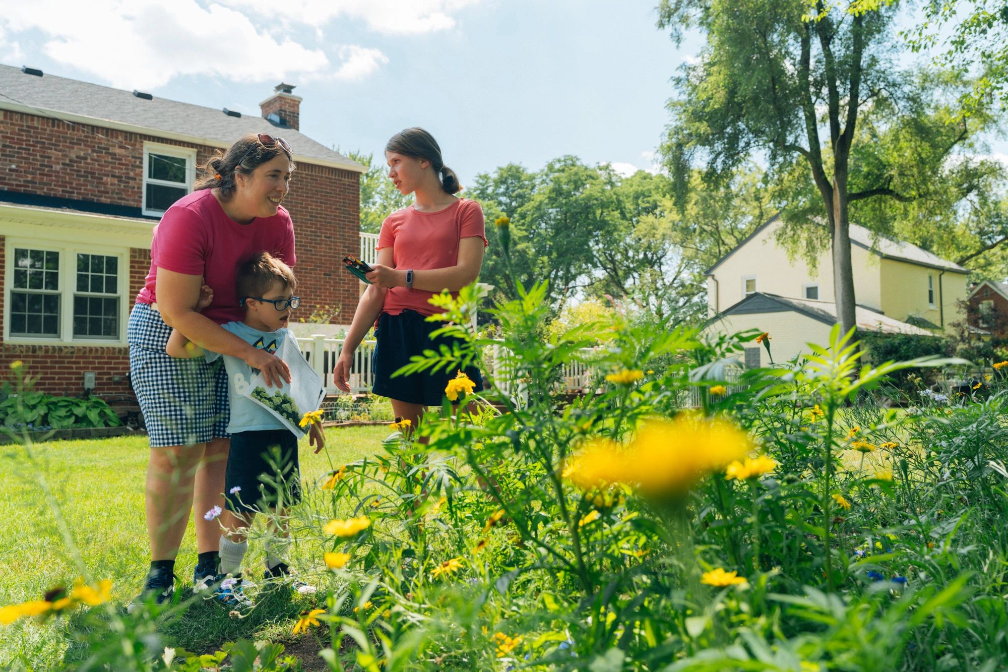 Three people enjoying a sunny day in a garden with yellow flowers.