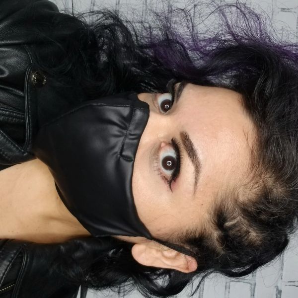 Person with dark curly hair wearing a black face mask and leather jacket.