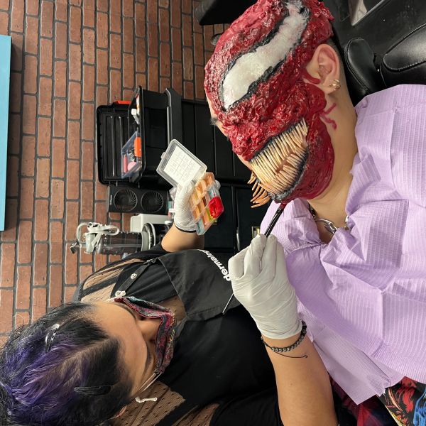 Artist applying detailed makeup effects to create a monster face with sharp teeth.