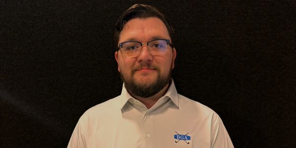 Man in white polo shirt with BGA logo posing against dark background.