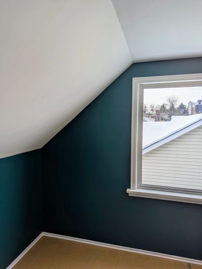 Small room with slanted ceiling, dark teal walls, and a window overlooking snowy rooftops.