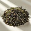A pile of loose black and green tea leaves on a white surface.
