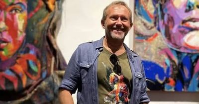 Man smiling in front of colorful paintings.