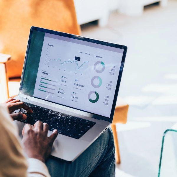 A person uses a laptop to view a dashboard with financial reports, charts, and graphs.