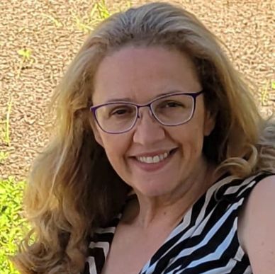 Smiling woman with glasses and wavy blonde hair.