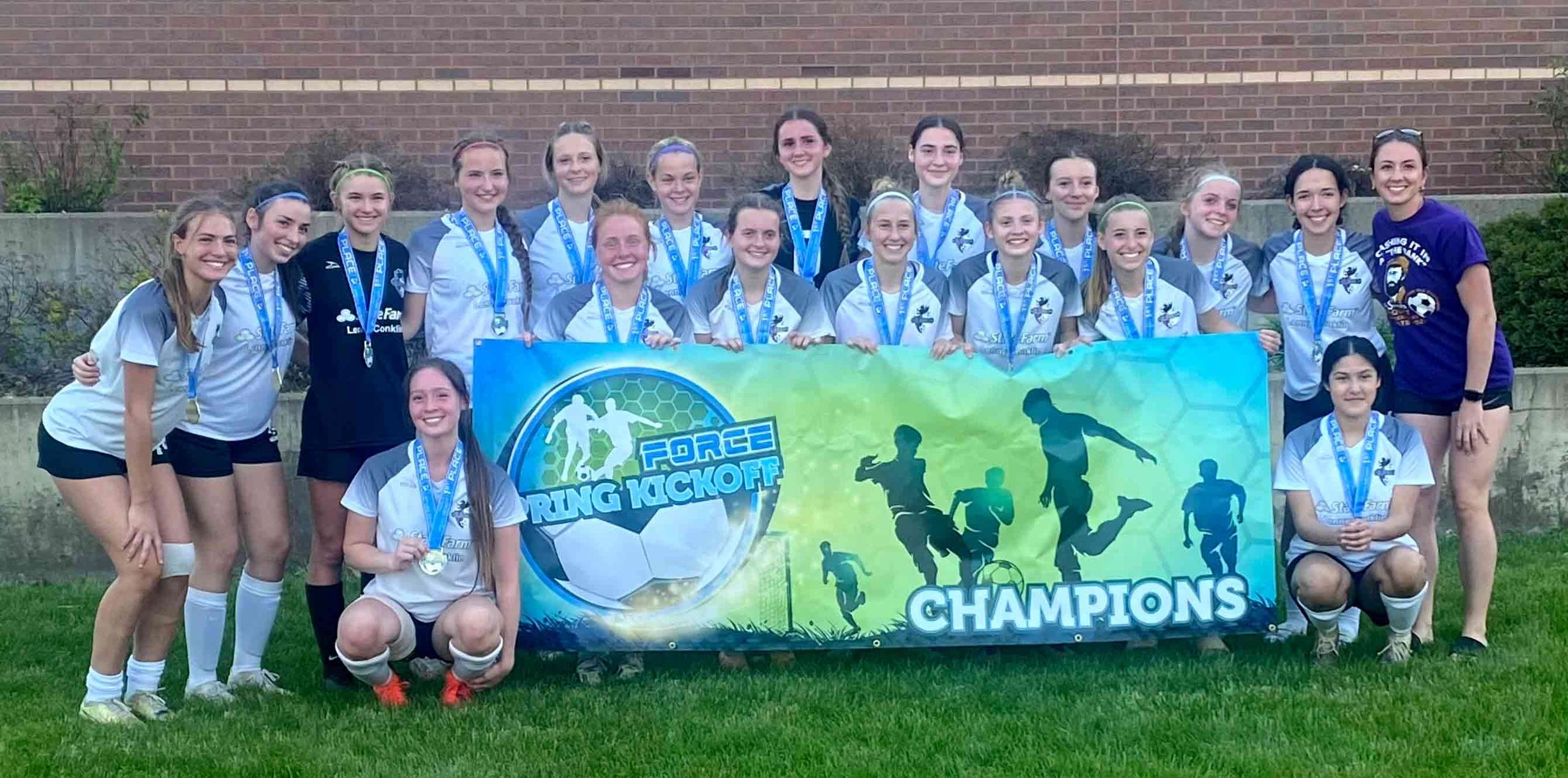 Girls' soccer team proudly poses with their championship banner and medals.