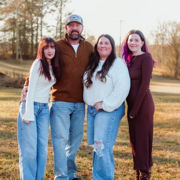 Family of four posing outdoors on a sunny day.