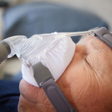 Man lying in bed wearing CPAP mask cushion with cover on it. 