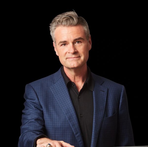 Portrait of a confident middle-aged man with gray hair against a black background.