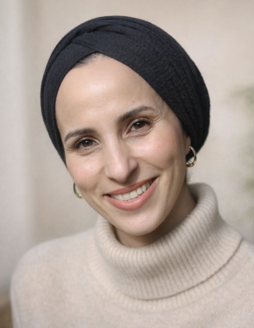 Portrait of psychotherapist Amna Rahim wearing a black head wrap and beige knit jumper in a calm neutral setting.