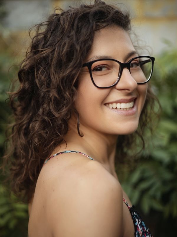 Smiling woman with curly hair and glasses in a floral dress.