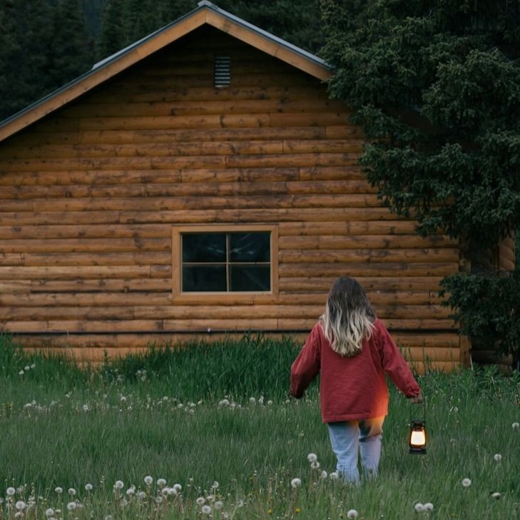 Child holding lantern walking toward cabin in woods Safe Harbor Counseling of Missouri logo