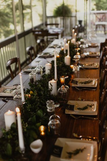 A wedding table with a harvest table, cross-back chairs, greenery, and candles.
